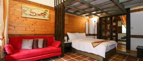 A room with a wooden ceiling, a red sofa, a bed with white bedding, and a tiled floor.