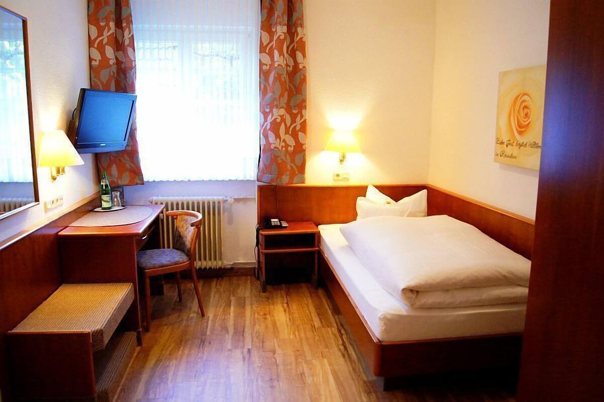 A hotel room with a bed, a desk with a chair, a television, and a nightstand with a lamp.