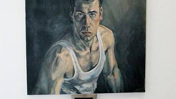 A painting of a muscular figure in a white tank top hanging on a white wall.