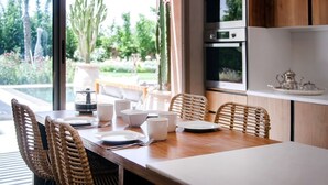 A dining area with a wooden table set for four, wicker chairs, and a view of a garden with a cactus. - Palais Sohan (Oulad Hassoune)