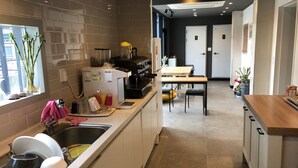A modern kitchen with a built-in coffee machine, a sink with dish drying rack, and a dining area with a table and chairs. - YH GuestHouse - Hostel (Seoul)