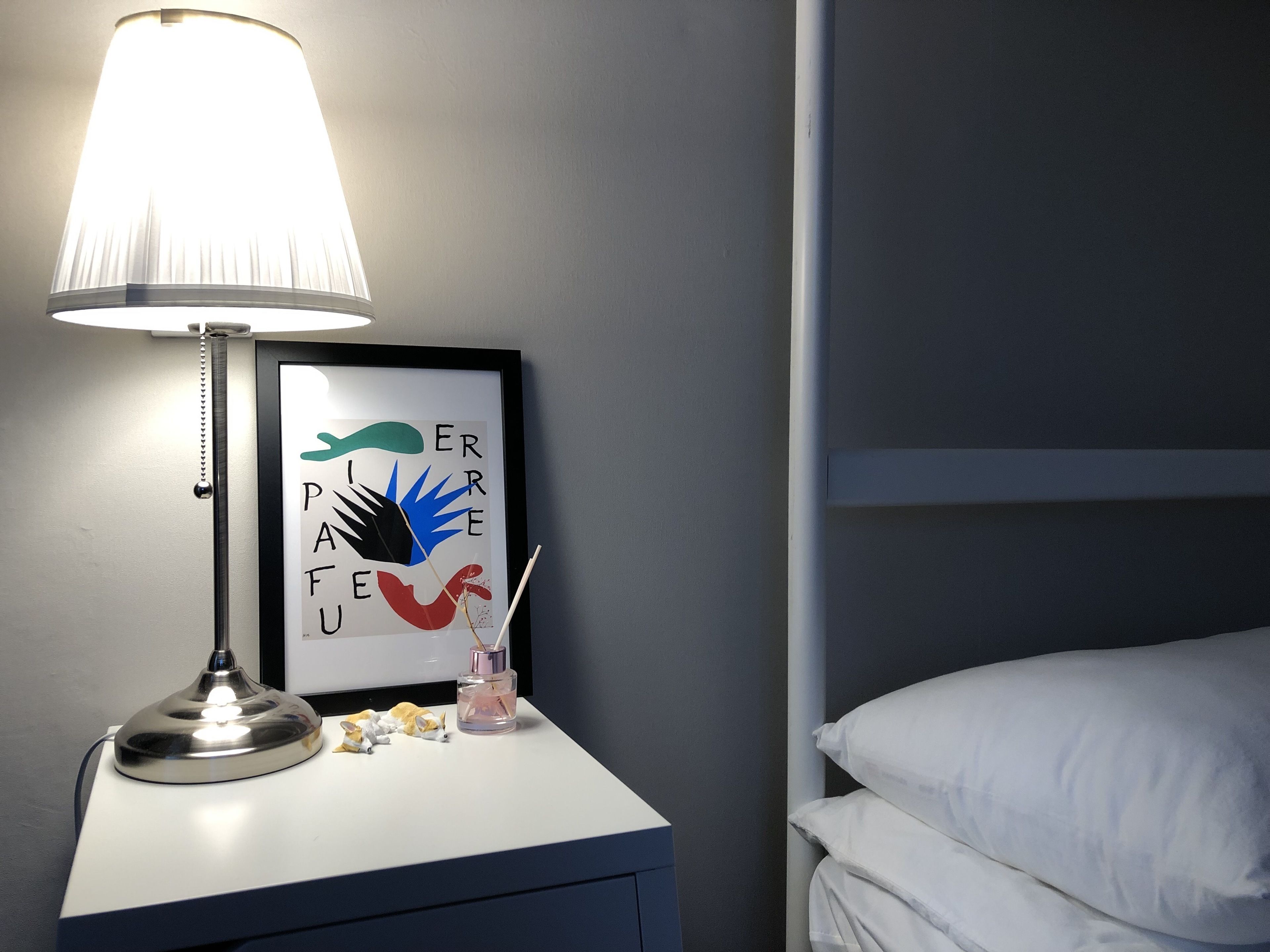 A bedside table with a lamp, a framed artwork, and a bottle of water.