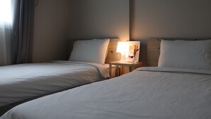 A hotel room with two beds, a bedside table with a lamp, and a window with curtains. - YH GuestHouse - Hostel (Seoul)