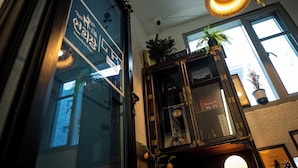 A room with a large window, a wooden cabinet with a plant, and a hanging light fixture. - YH GuestHouse - Hostel (Seoul)