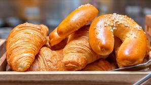 A wooden basket filled with various types of bread, including croissants and pretzels. - Pension Einsiedl (Ottenschlag)