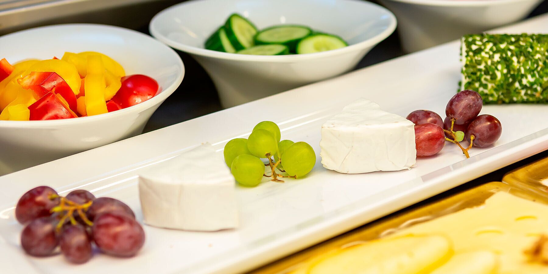Una tabla de quesos con distintos quesos, uvas y verduras en rodajas.
