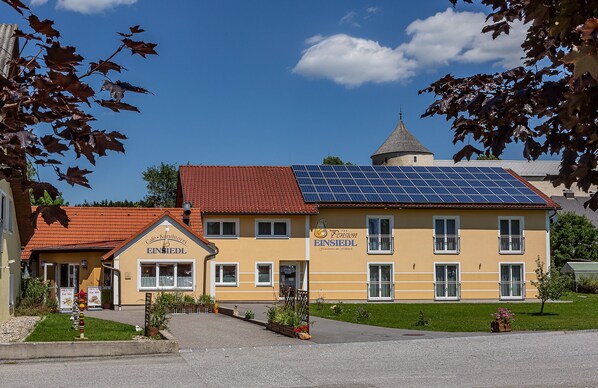 A two-story building with a red roof and a solar panel array on the roof. The building has a sign that reads "Fission EINSIEDL."