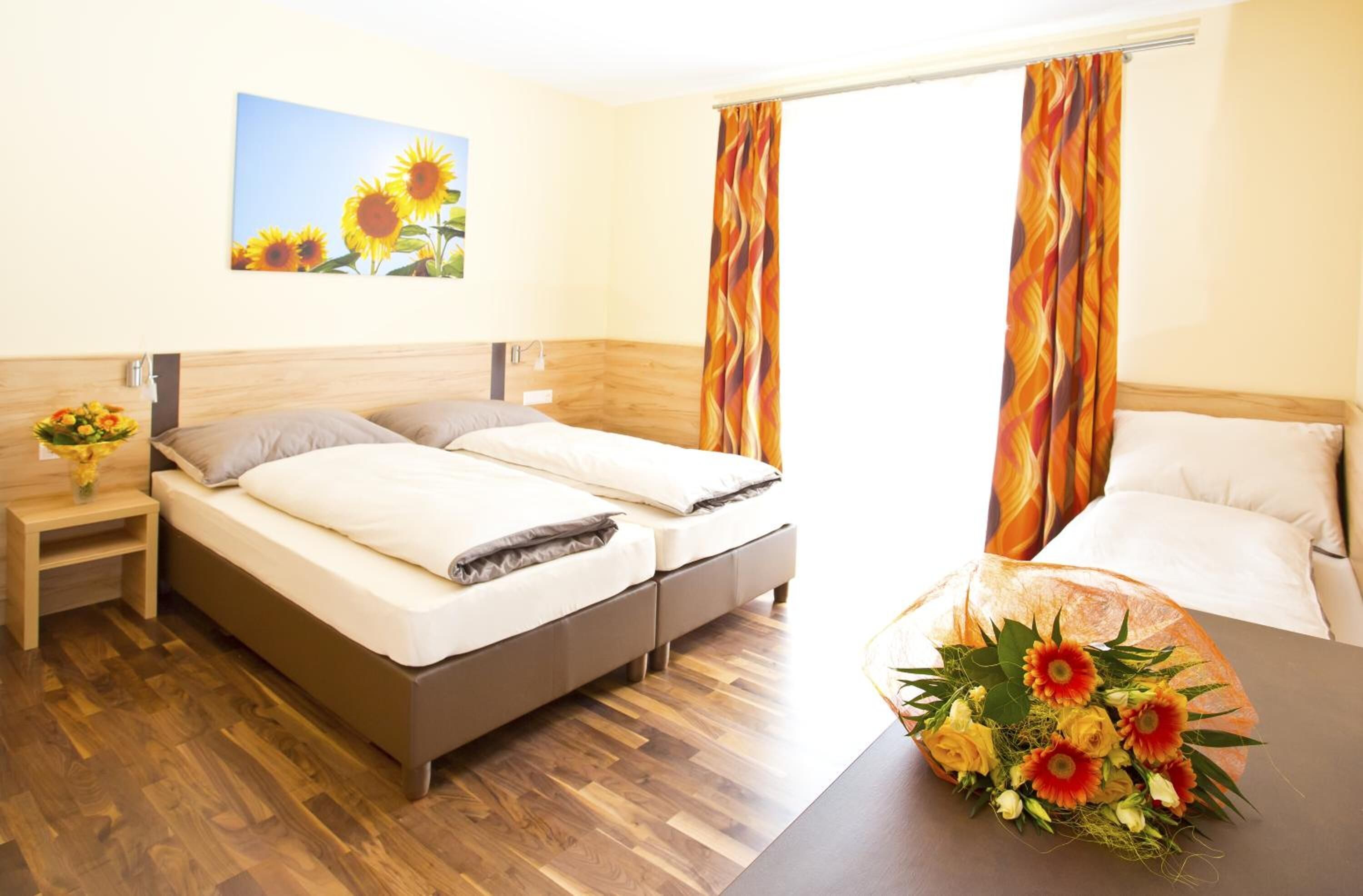 A hotel room with a wooden bed, a nightstand with a vase of flowers, and a painting of sunflowers on the wall.