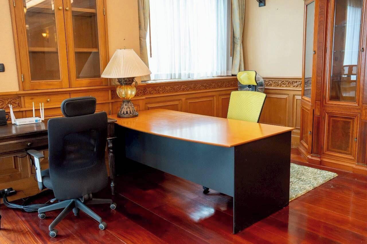Ein Konferenzraum mit einem Holztisch, zwei Stühlen, einer Lampe und einem Fenster mit Vorhängen.