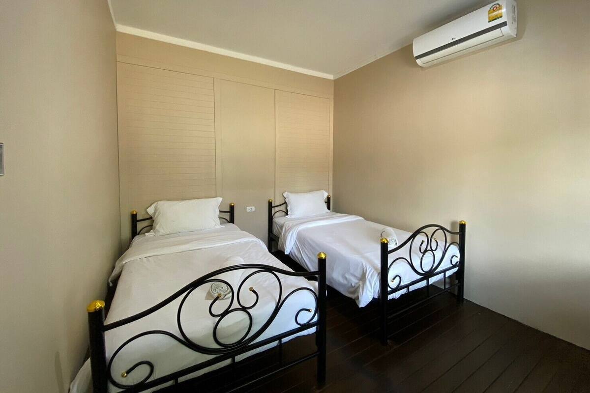 A room with two single beds, a ceiling-mounted air conditioner, and a plain wall.