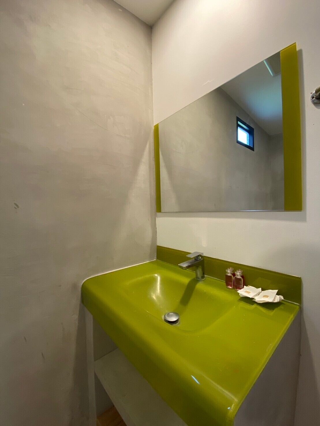 A bathroom with a green sink, a mirror, and a small window.