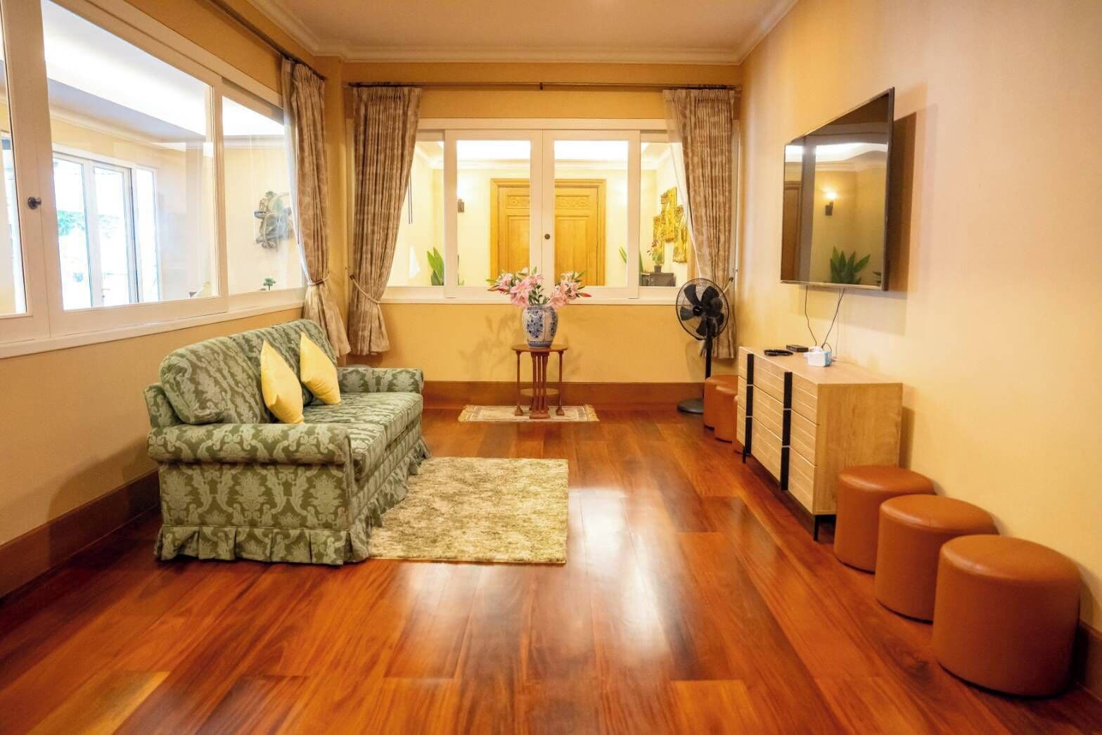 Una sala de estar con un sofá, una mesita con un florero, un ventilador y un televisor sobre un mueble bajo.