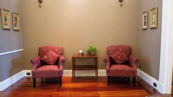 Une pièce avec deux fauteuils rouges, une petite table d’appoint en bois sur laquelle est posée une plante, et un mur beige orné de tableaux encadrés.