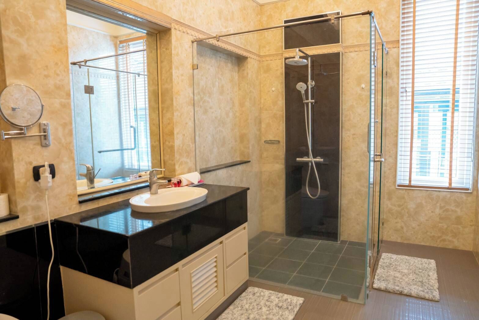 A modern bathroom with a glass-enclosed shower, a black countertop, and a beige tiled floor.