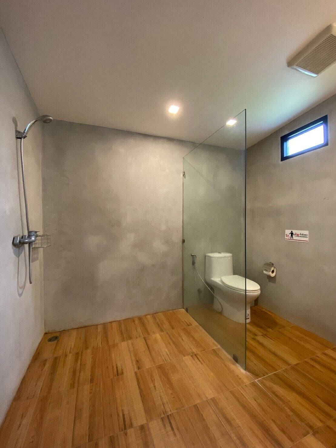 A modern bathroom with a glass shower enclosure, a toilet, and a wooden floor.