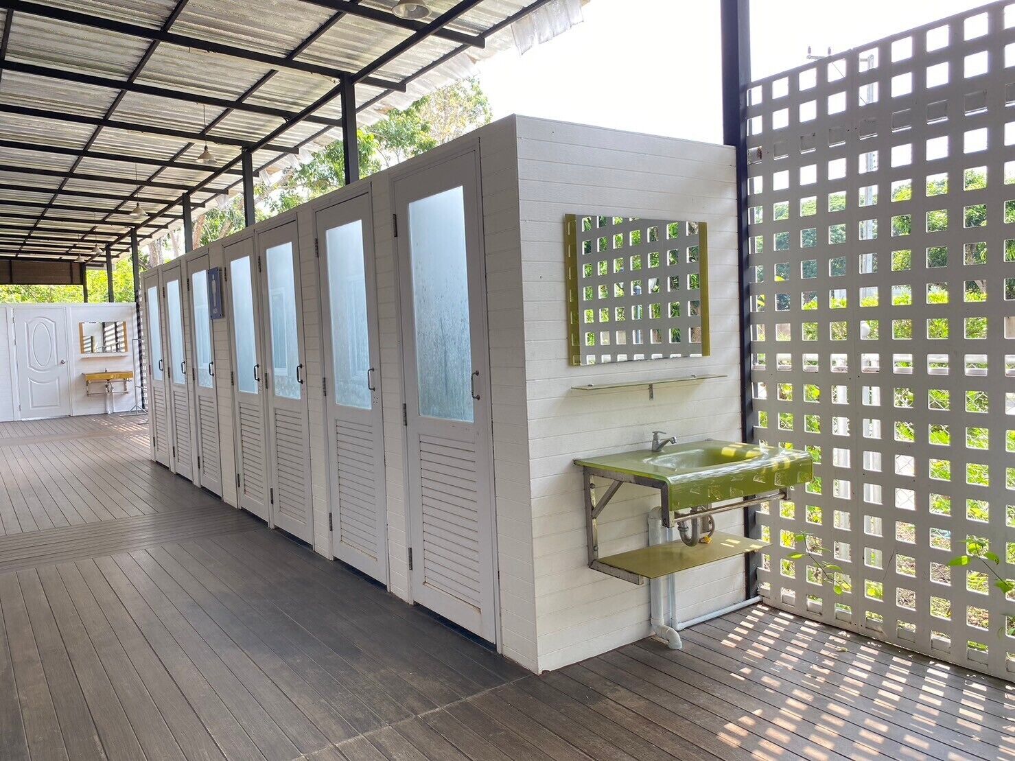 Una fila de taquillas blancas con puertas de vidrio satinado, un lavamanos metálico de tonalidad verdosa y una pared blanca con un panel de vidrio decorativo.