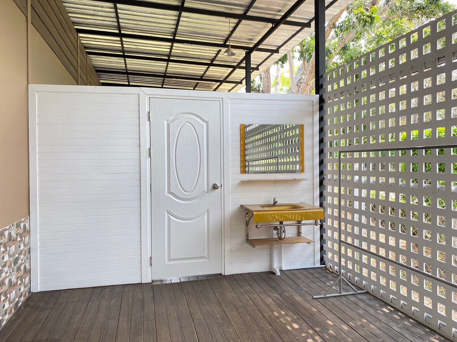Un espace extérieur abrité, doté d’une porte blanche, d’un petit lavabo et d’une clôture en métal.