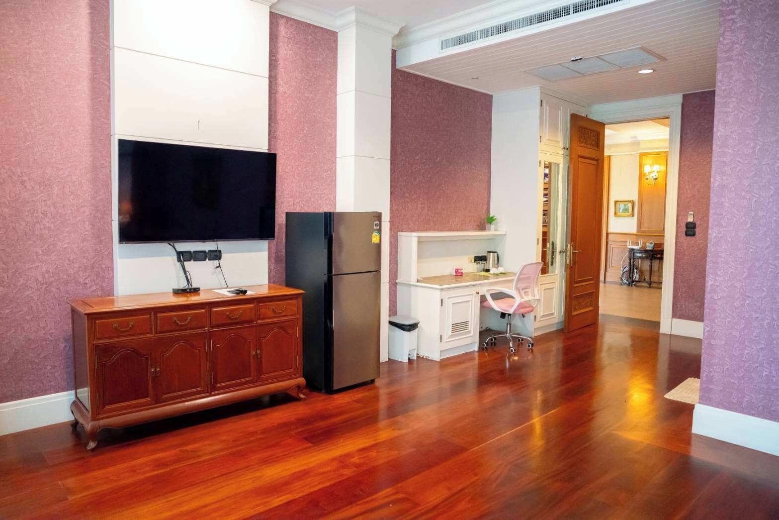 A compact kitchen with a wooden cabinet, a black refrigerator, a white countertop, and a pink chair.