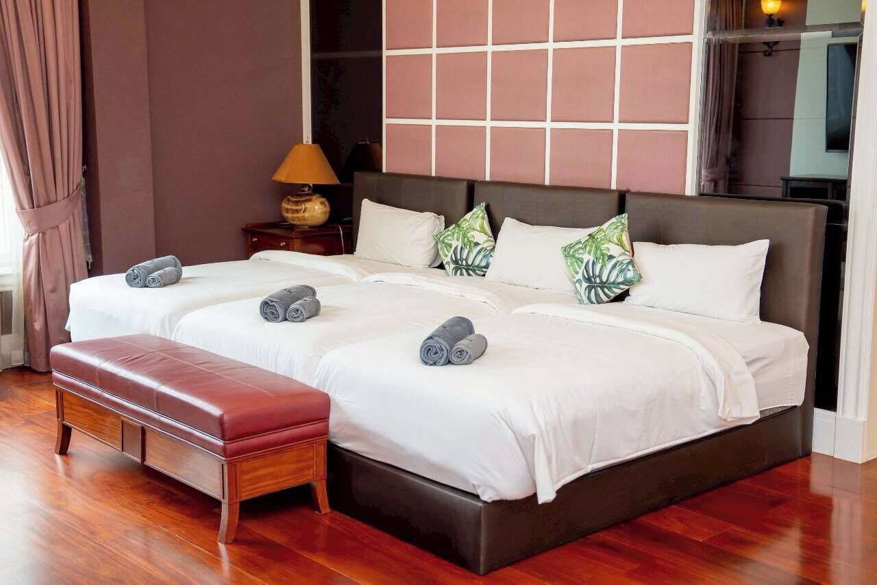 A double bed with a wooden bench, a nightstand with a lamp, and a decorative wall panel.
