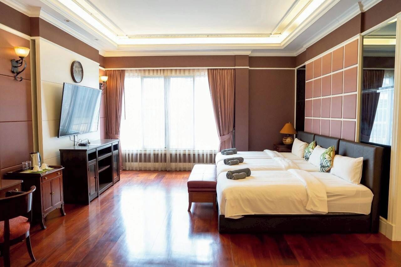 A hotel room with a large bed, a TV, a desk, and a window with curtains.