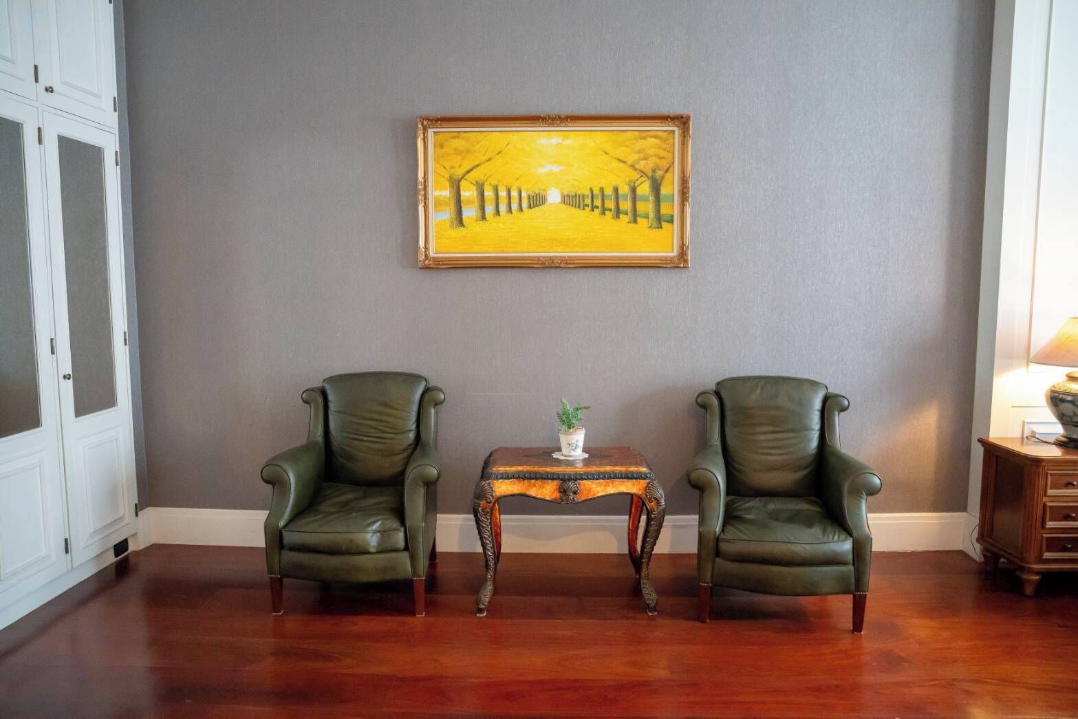 Een kamer met twee lederen fauteuils, een tafeltje met een plant en een schilderij aan de muur.