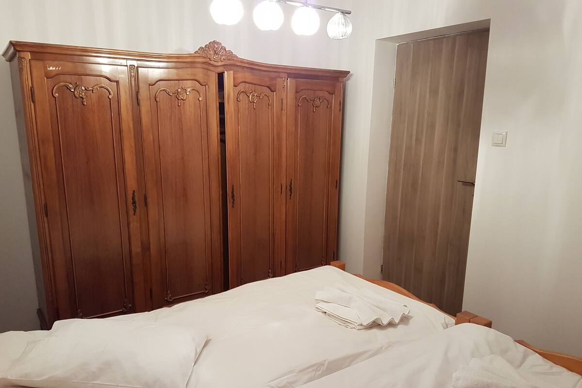 A bedroom with a wooden wardrobe, a bed with white bedding, and a closed door.