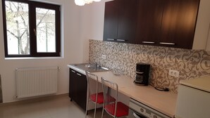 Een kleine keuken met een raam, een spoelbak, een koffiezetapparaat en een fornuis.