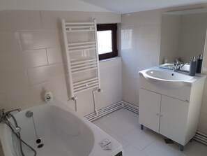 Un baño moderno con bañera, un lavabo blanco con espejo y un perchero para toallas.