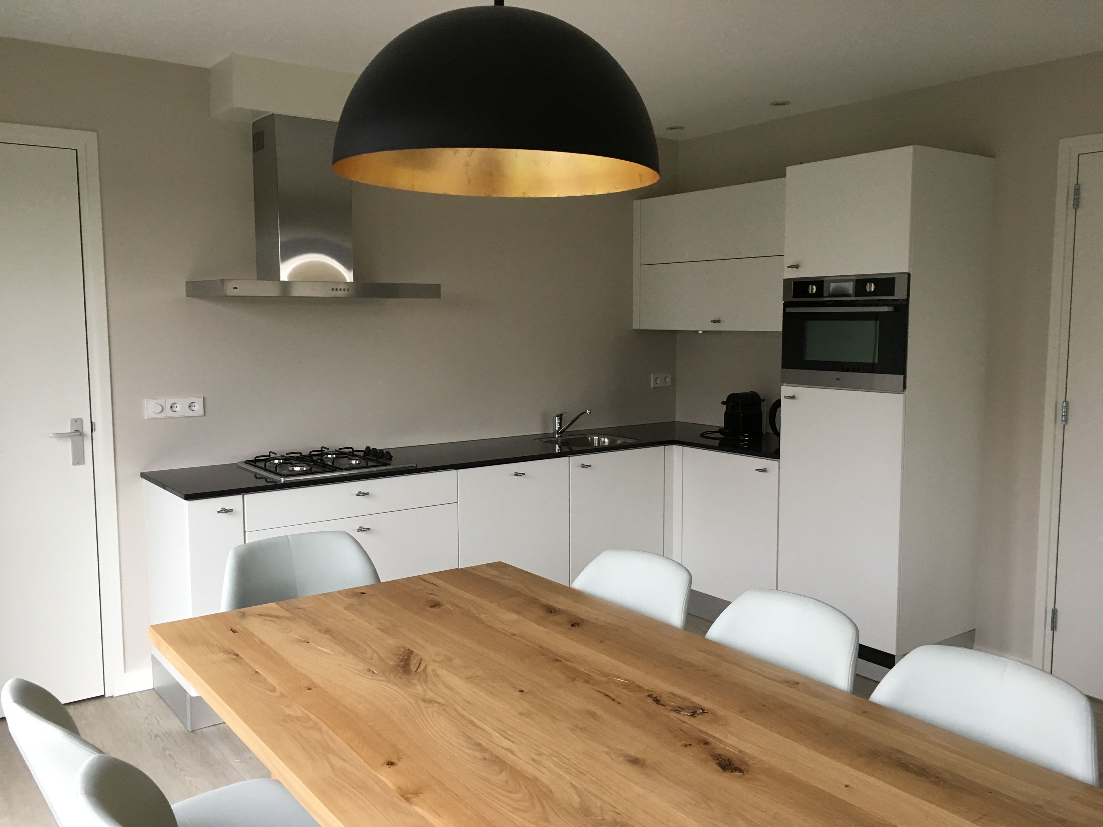 Una cocina moderna con armarios blancos, encimera negra y una mesa de comedor de madera con sillas.