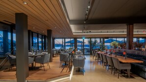 A modern restaurant with a wooden ceiling, large windows, and a view of mountains. - Oesterdam Resort (Tholen)