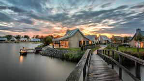 A lakeside property with wooden houses, a dock, and a wooden bridge. - Oesterdam Resort (Tholen)
