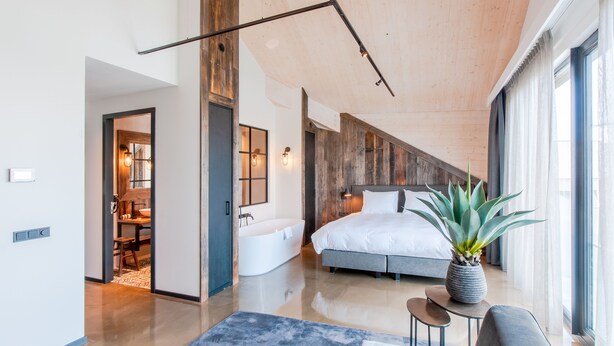 A modern bedroom with a large bed, a bathtub, and a dining area. - Oesterdam Resort (Tholen)