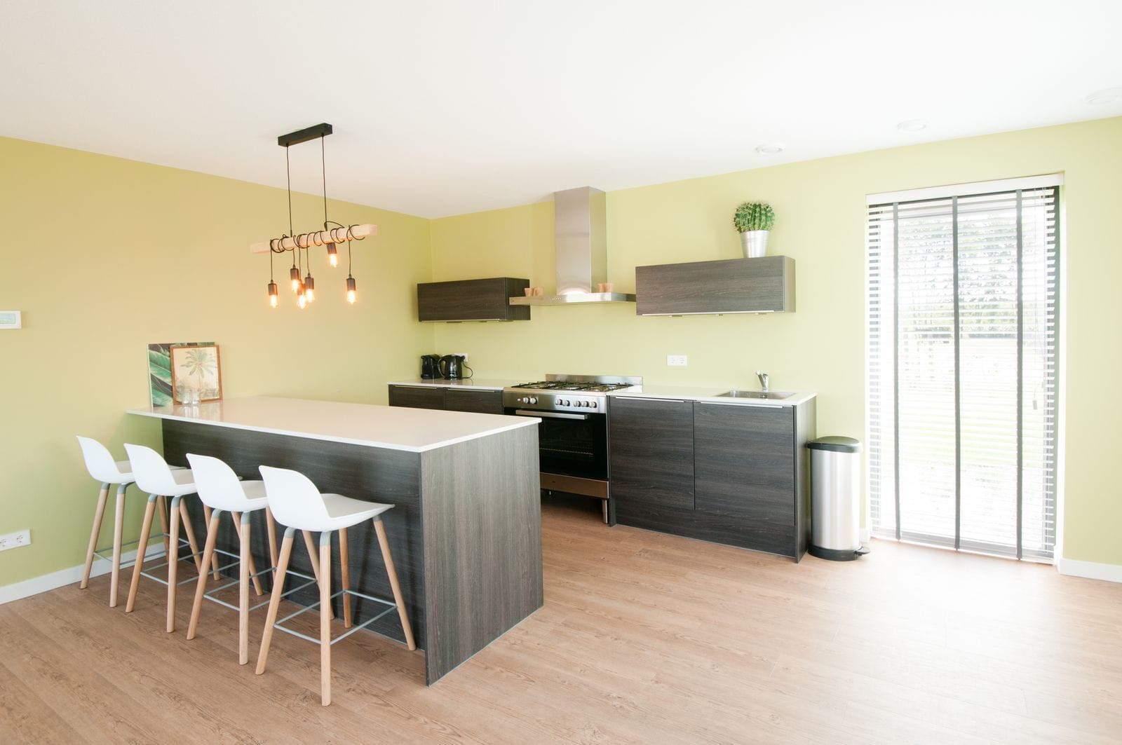 A modern kitchen with a central island, bar stools, a stove, and a trash can.