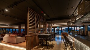 A modern bar area with a bar counter, stools, and a seating area with a sofa and chairs. - Oesterdam Resort (Tholen)