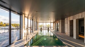 A modern indoor swimming pool with glass walls, large windows, and a view of boats outside. - Oesterdam Resort (Tholen)