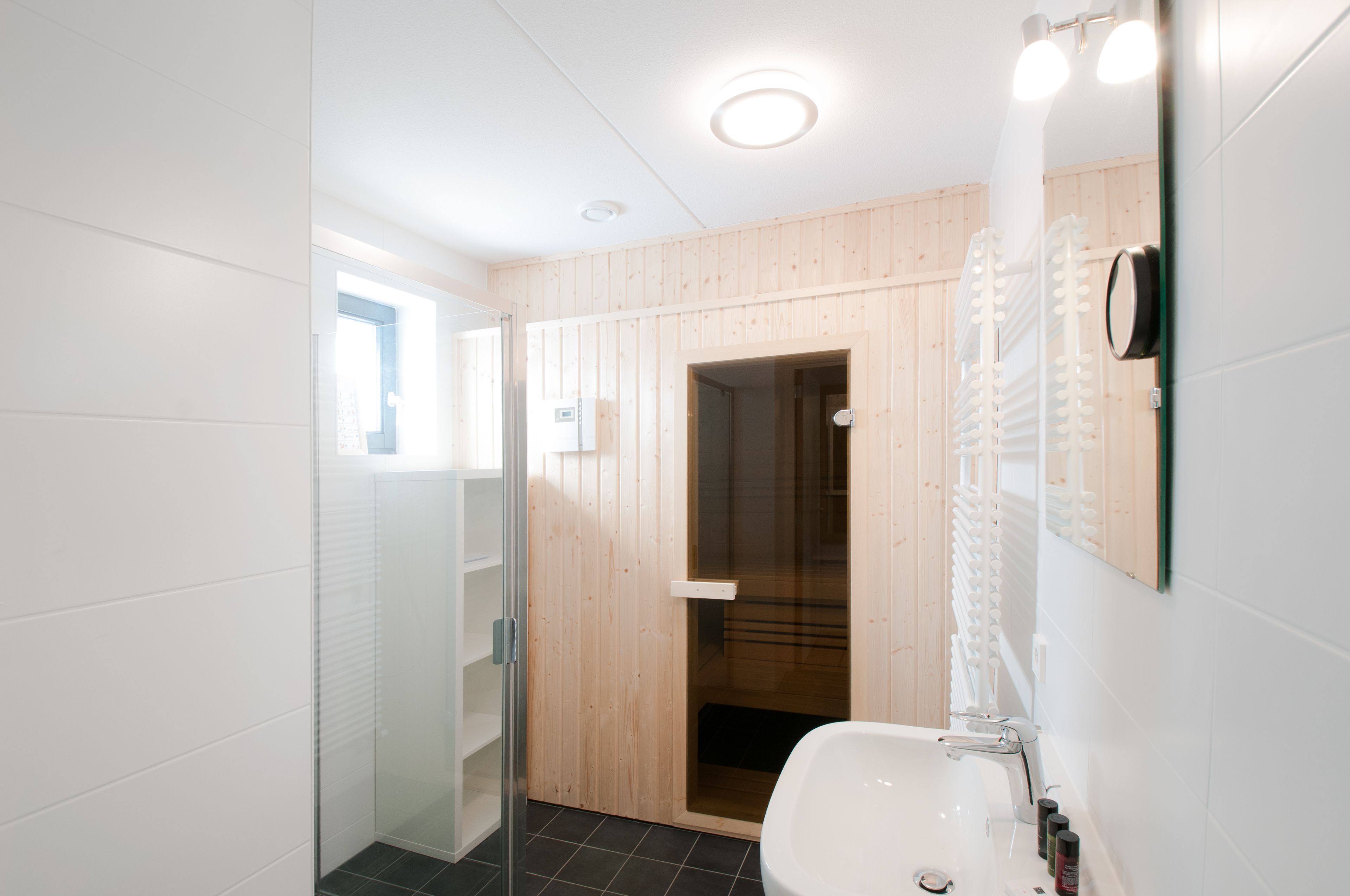 Un baño moderno con cabina de ducha de vidrio, pared revestida de paneles de madera y lavamanos blanco con espejo.