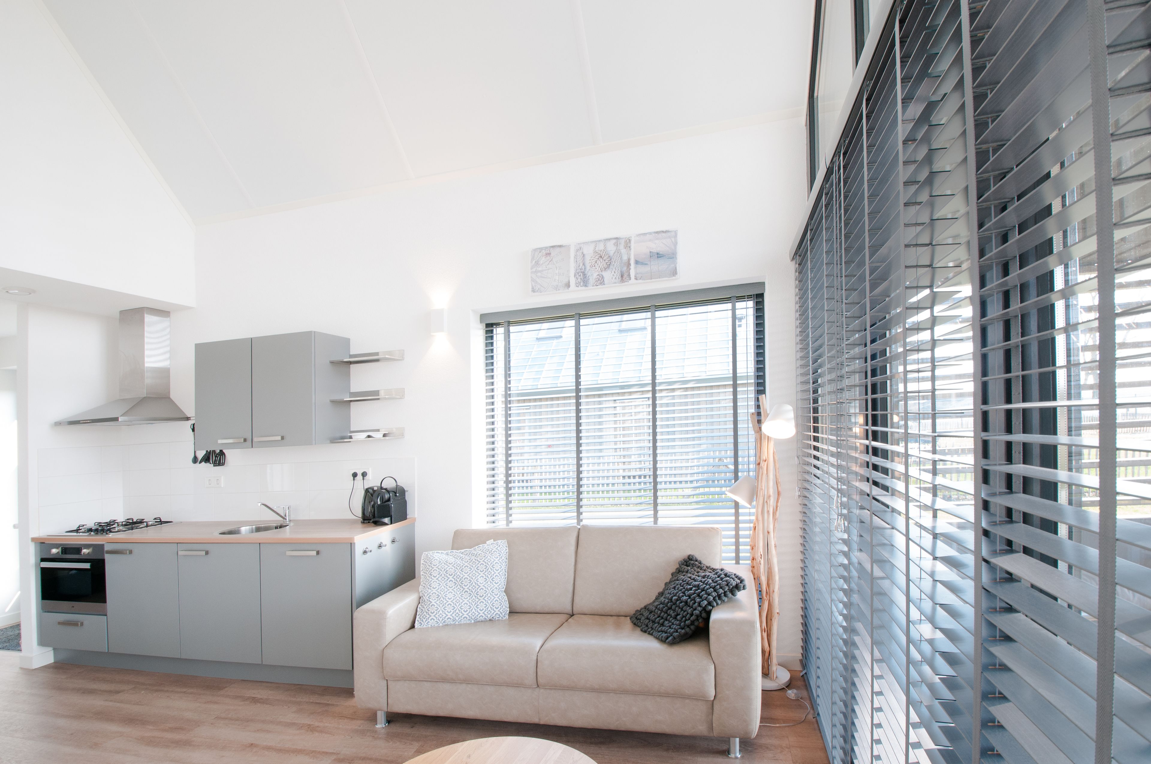 A modern kitchen with grey cabinets, a beige sofa, and a large window with blinds.