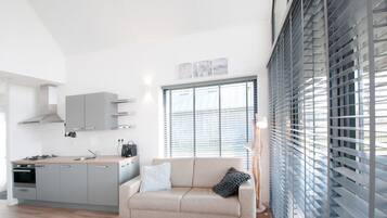 A modern kitchen with grey cabinets, a beige sofa, and a large window with blinds.