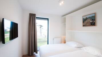Une chambre avec un grand lit, un téléviseur fixé au mur, une fenêtre avec des rideaux et un tableau accroché au mur.