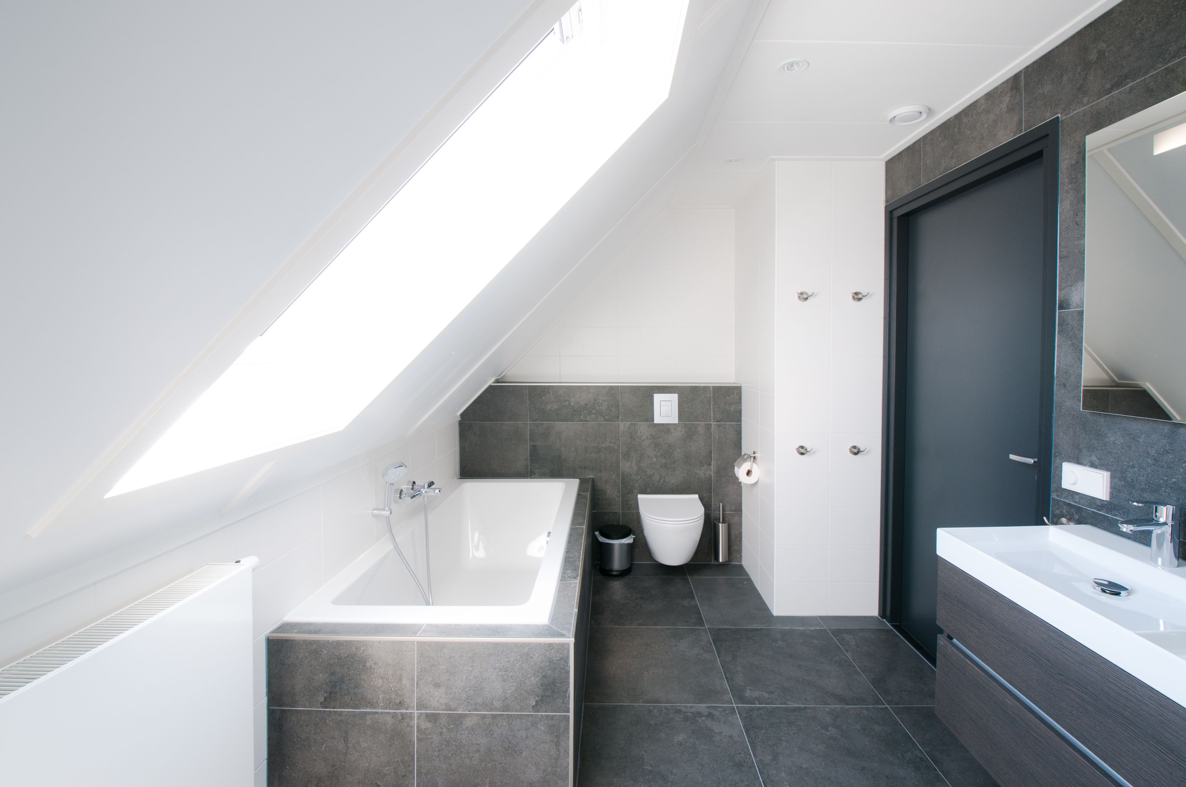 A modern bathroom with a skylight, a bathtub, a toilet, and a large mirror.