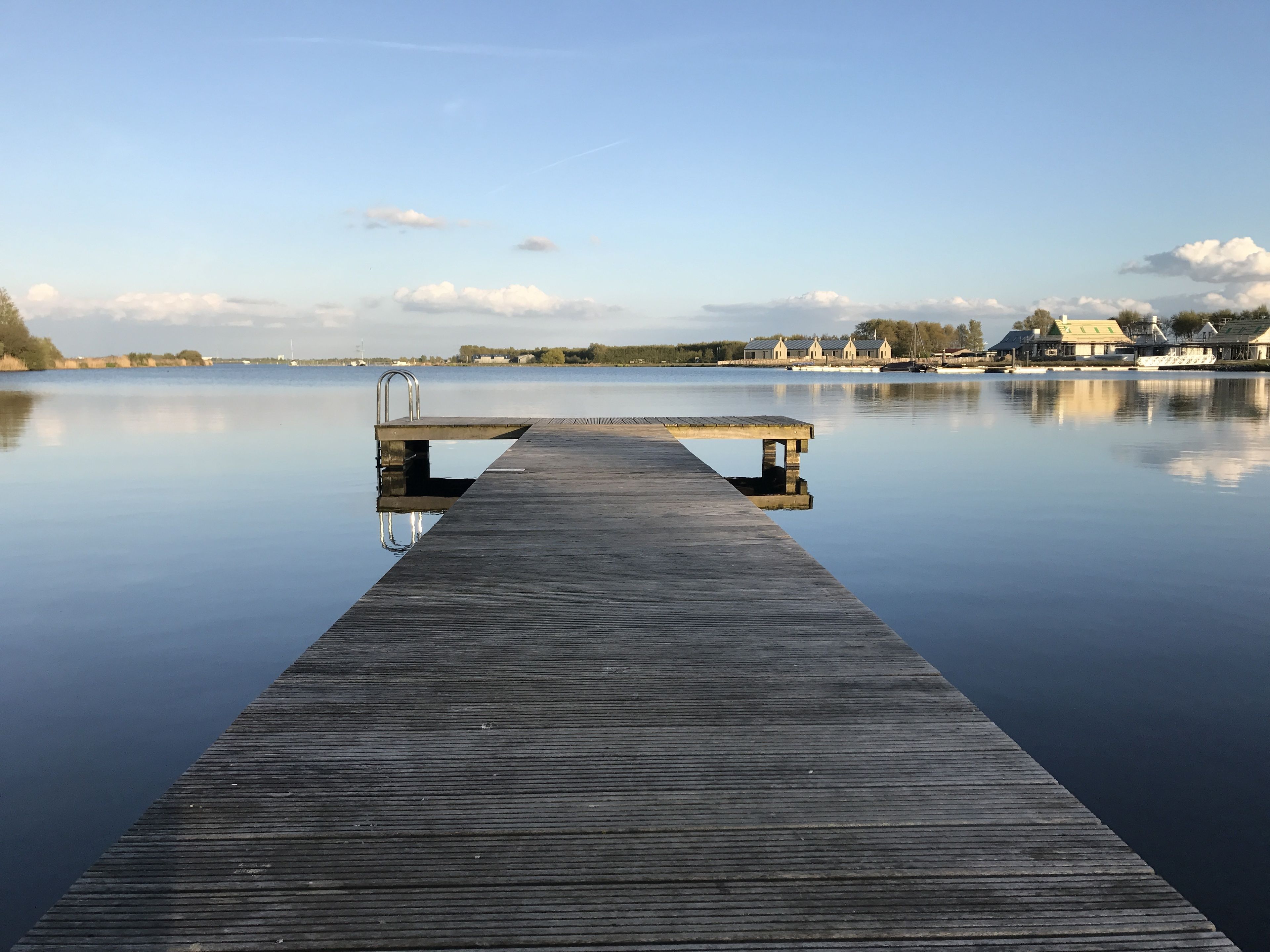 A wooden pier extending into calm water with a metal ladder at the end.