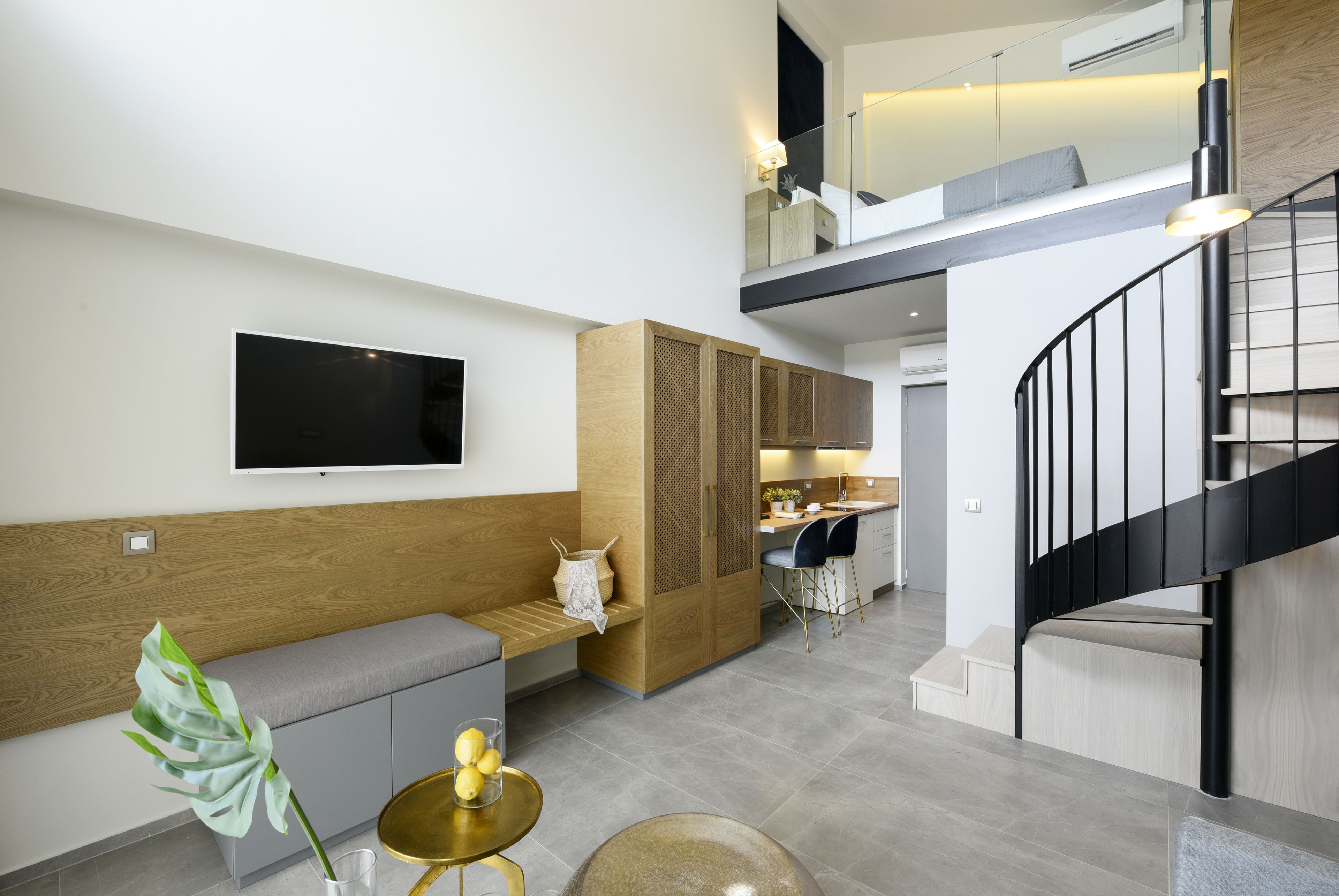 A modern living area with a sofa, a TV mounted on the wall, a staircase, and a kitchen in the background.