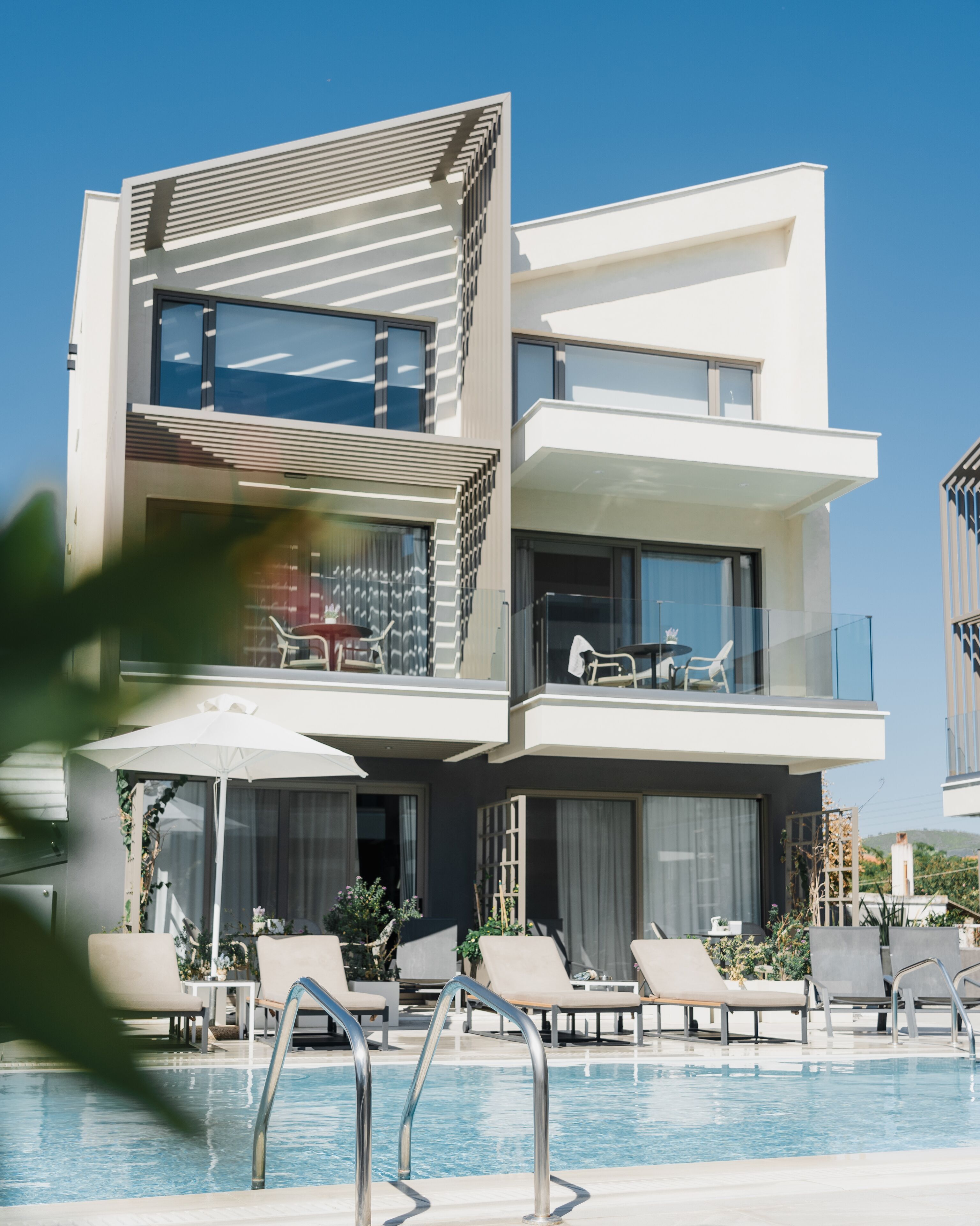 A modern multi-story hotel with a pool area, including lounge chairs and umbrellas.
