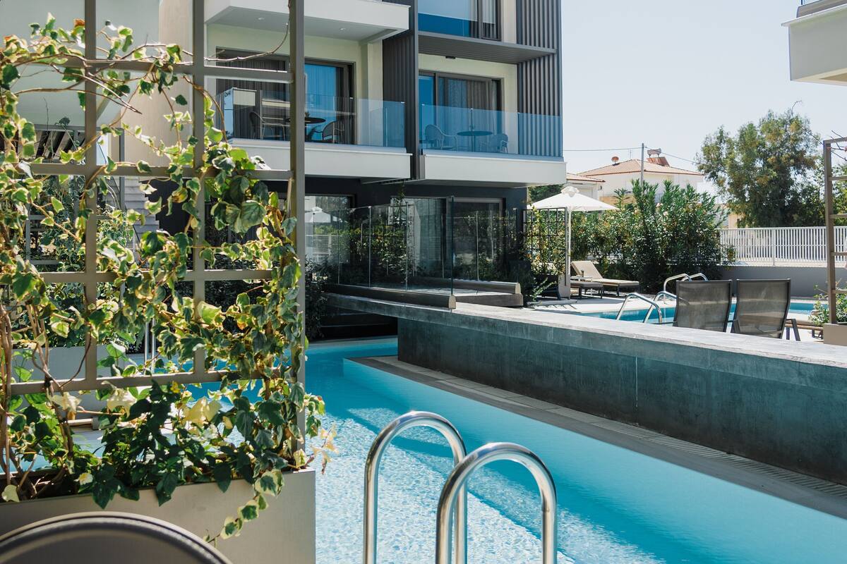 Un área de piscina moderna con una piscina azul cristalina, barandales de metal y vistas a un edificio contemporáneo con balcones.