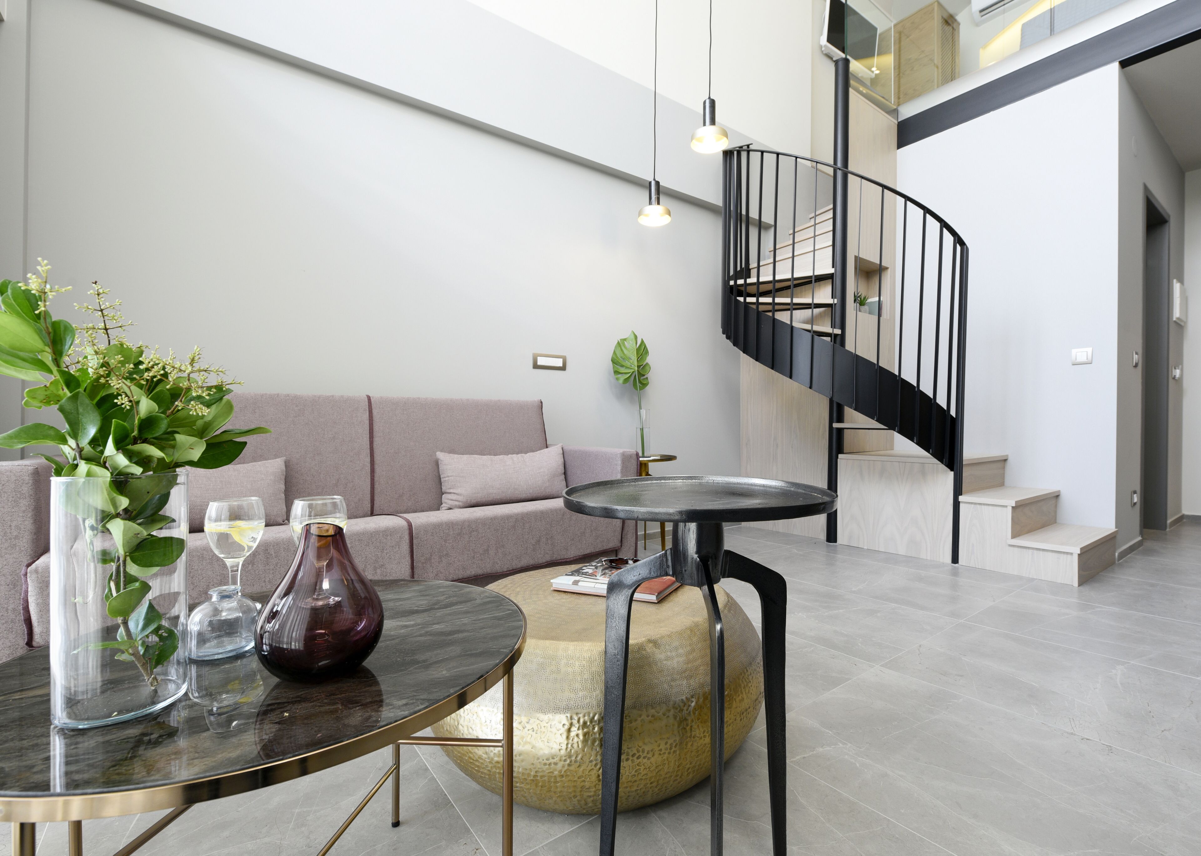 Ein modernes Wohnzimmer mit einem runden Glastisch, einer Couch, einem Blumentopf und einer Wendeltreppe.