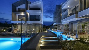 A modern hotel with a swimming pool, outdoor seating, and a well-lit exterior. - Serenity Suites (Nikiti)