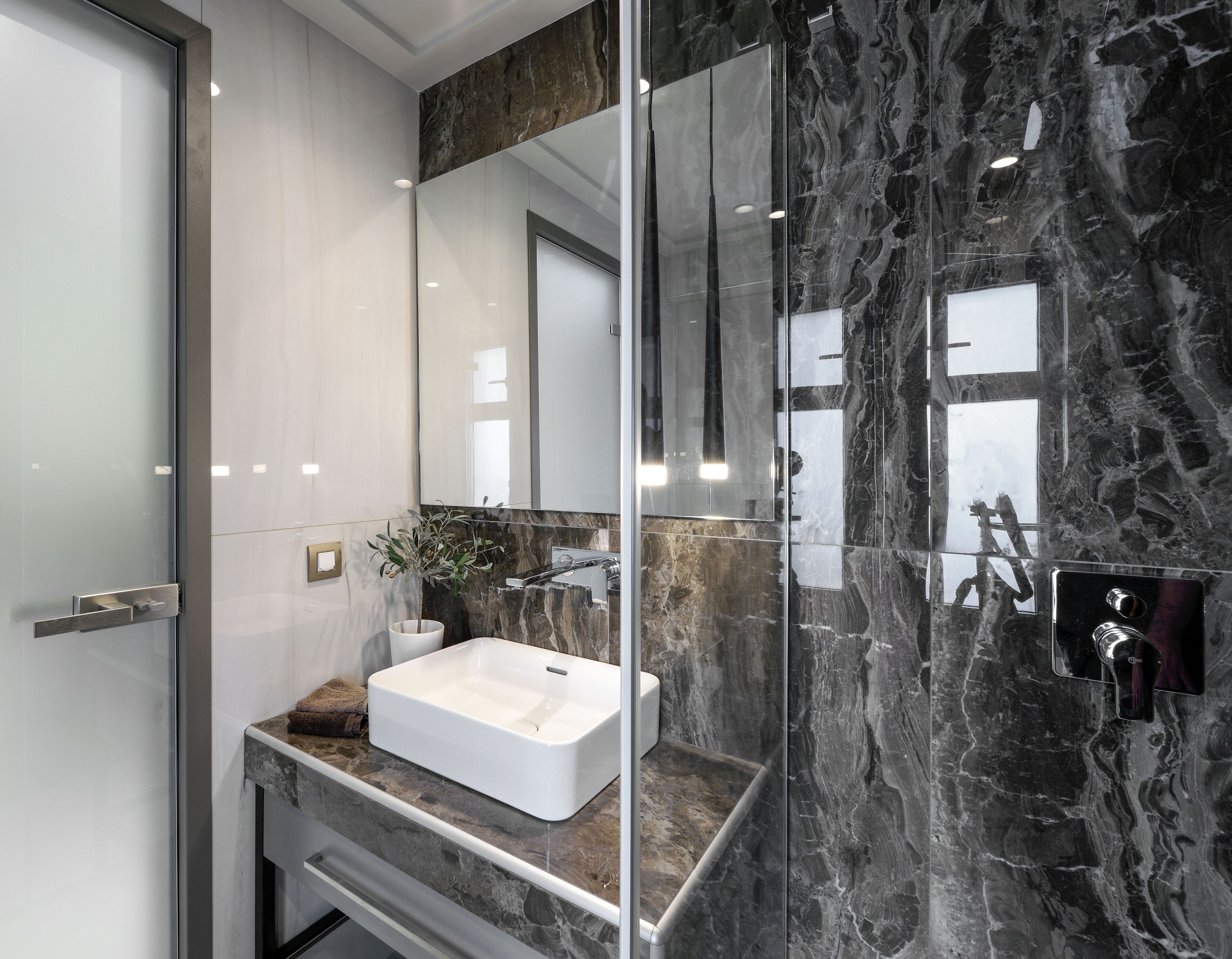 A modern bathroom with a white sink, marble backsplash, and a large mirror.