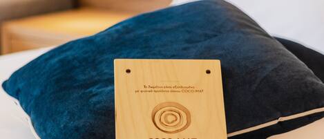 Una cama con una almohada azul oscuro y una placa de madera con la inscripción "COCO-MAT sleep on nature" en una habitación de hotel.