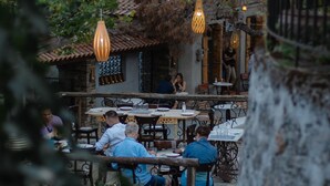 An outdoor dining area with tables and chairs, surrounded by trees and a stone wall. - Serenity Suites (Nikiti)