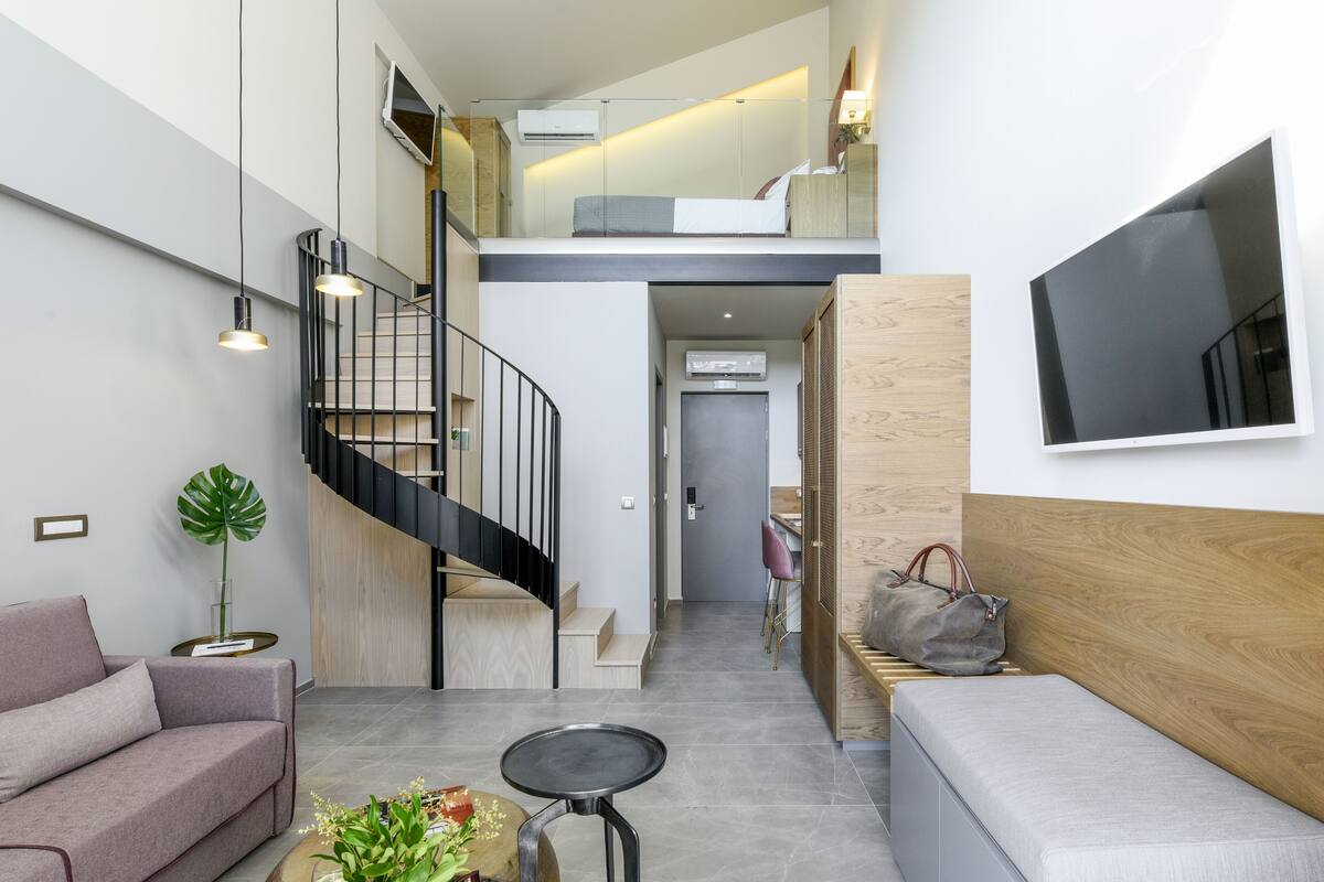 Un interior moderno con una escalera, un sofá, una mesa de centro y un televisor montado en la pared.